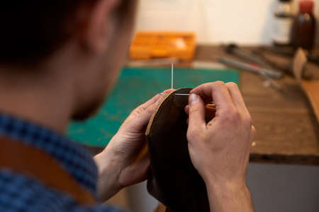 The leatherman threading needle for leather working. Closeup of male hands sewing leather parts with...