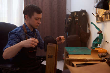 The craftsman sewing leather parts with the needle. A small business of a craftsman. The craftsman...