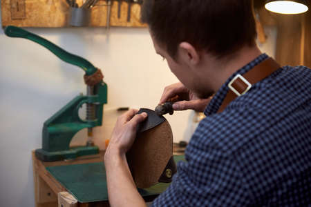 The leatherman holding crafting tool and working with genuine leather. Closeup of craftsman working...