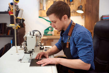 The man behind sewing machine. The room with white table, sewing machine on it and working man....
