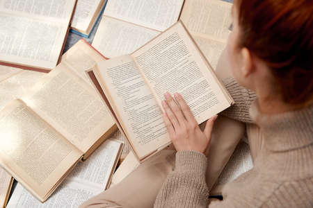 Closeup photo of a girl with a book in her hands sitting around many books. Distance learning. Home schooling. Self-education during quarantine.の写真素材