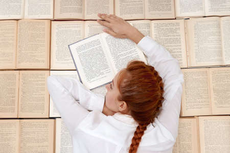 Student girl is tired of quarantine and self-isolation. A red-haired girl lies among many books....