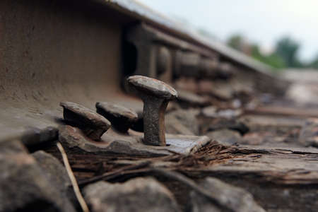 Detail of rusty screws on railroad track. Wooden tie with rusty nuts and bolts. Single rail as part of a railway. Close up of old abandoned rusty rails with wooden sleepers.の写真素材