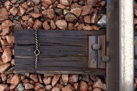 Detail of rusty screws on railroad track. Wooden tie with rusty nuts and bolts. Single rail as part...