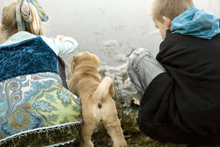 Brother and sister playing at the lake while sharpei puppy is watchingの写真素材
