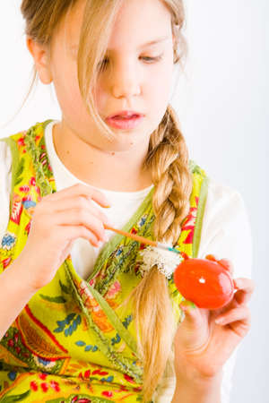 Studio portrait of a young blond girl who is painting an egg red for easterの写真素材