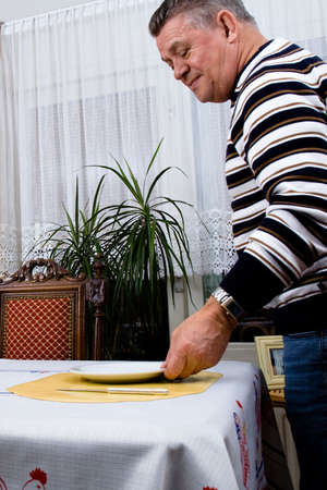 Senior man is preparing the breakfast tableの写真素材