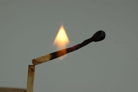 A mburning matchstick isolated against a gray background