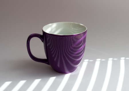 cup on a white table with shadows from the blinds incidentの写真素材