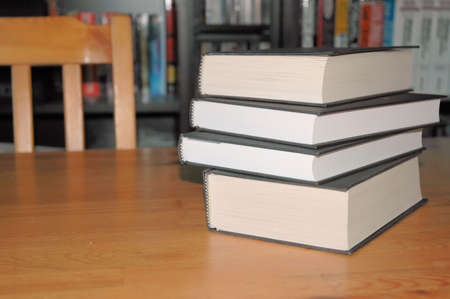 Stack of books on a table with book shelf in the background
