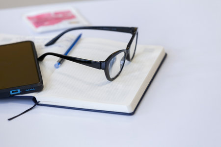 Glasses, smartphone and notepad on the desktop. Work or workplace concept. Selective focus.