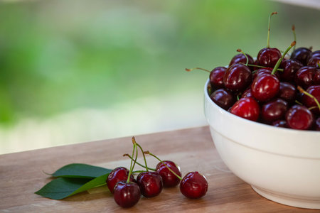 Fresh Cherries with Stems and Leaves on Wooden Table, Bowl of Cherries in Background with Leafy...