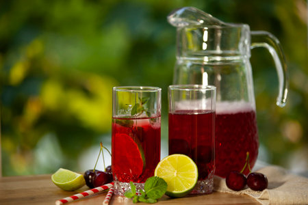 A glass pitcher of refreshing fruit punch, accompanied by two glasses garnished with lime, mint, and cherries. Horizontal photo.の写真素材