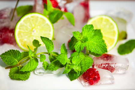 Bright lime slice with mint leaves and berry ice cubes. Summer freshness and color in a macro food...