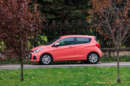 Compact pink car in urban park. Pink city car parked near trees and green grass. Urban mobility, eco transport, and colorful modern lifestyle.の写真素材