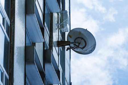 Satellite dish on building facade. Satellite dish installed on tall building against blue sky,...