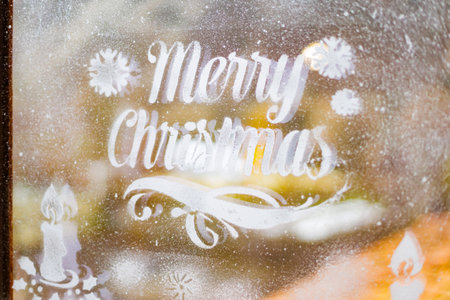 Cozy frosted window with Christmas message. Frosted window with Merry Christmas lettering and candle decorations.の写真素材