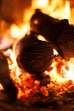 Burning logs in fireplace. Close-up of glowing firewood and bright orange flames inside a fireplace - cozy warmth and winter comfort.の写真素材