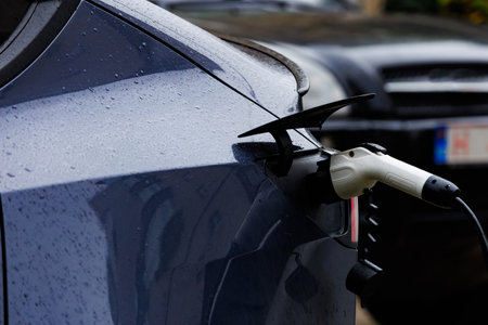 Electric car charging in rainy weather from rear view. Rear close-up of an electric car plugged into...