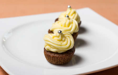 Three chocolate cupcakes with silver sprinkles on top, on white plate and fabric tableclothの写真素材