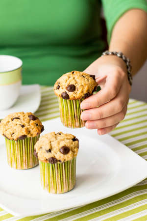 Nice girl hand taking delicious chocolate chip muffin at breakfast in green striped tableclothの写真素材
