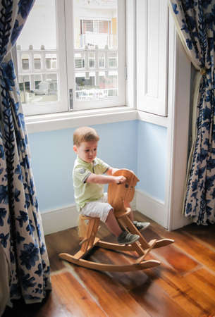 Cute little boy riding on vintage wooden rocking horseの写真素材