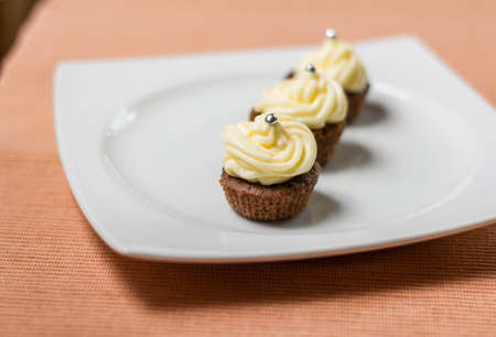 Three chocolate cupcakes with silver sprinkles on top, on white plate and fabric tableclothの写真素材