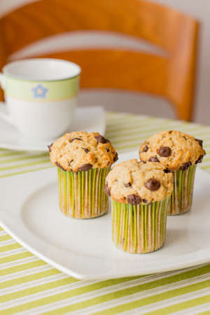 Three chocolate chip muffins on white plate and green striped tablecloth at breakfastの写真素材