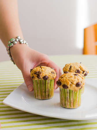 Nice girl hand taking delicious chocolate chip muffin at breakfast in green striped tableclothの写真素材