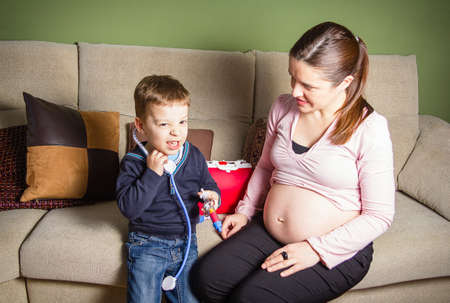 Funny child doctor examining his pregnant mother with medical  toys