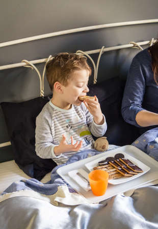 Happy mother and son having breakfast in bed at home in the morningの写真素材