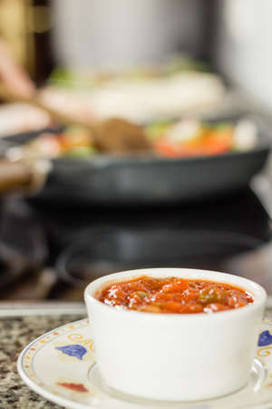 Closeup of bowl of hot sauce prepared for a mexican food and female cooking in a black pan in the backgroundの写真素材