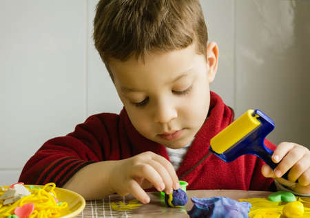 Cute child playing with colorful plasticine in a tableの写真素材