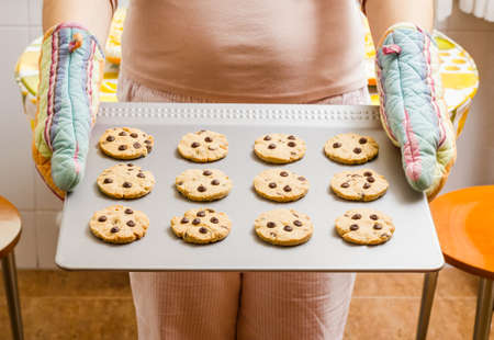 Woman holding a tray with homemade baked cookies with colorful kitchen glovesの写真素材