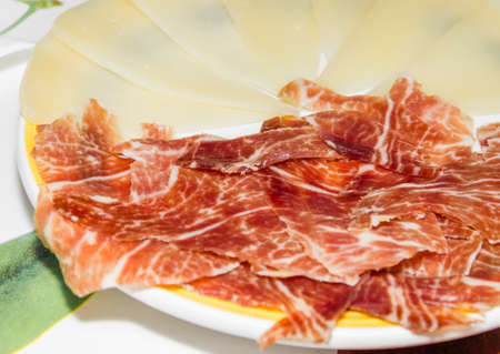 Closeup of typical spanish tapa, with slices of serrano ham and manchego cheese served in a plateの写真素材