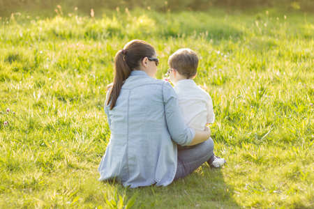 Back view of cute son giving a bouquet of flowers to his mother sitting in a sunny fieldの写真素材