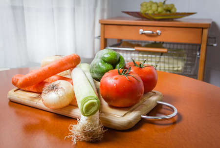 Fresh vegetables on cutting board in a wooden kitchen tableの写真素材