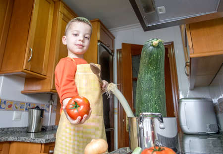 Cute child chef with apron cooking big zucchini and other vegetables in a pot on the kitchenの写真素材