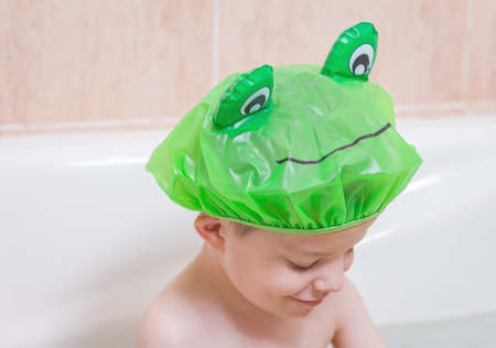 Cute boy happiness with a green cap having bath in bathtubの写真素材
