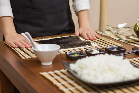 Woman chef ready to prepare japanese sushi rolls, with principal ingredients in the foreground  Selective focus in nori seaweed の写真素材