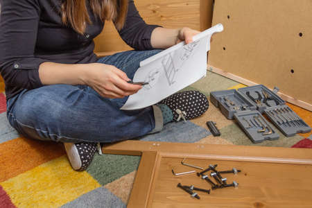 Closeup of girl with tools reading the instructions to assemble a new furniture for homeの写真素材