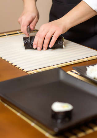 Closeup of woman chef cutting japanese sushi rolls with rice, avocado and shrimps on nori seaweed sheetの写真素材