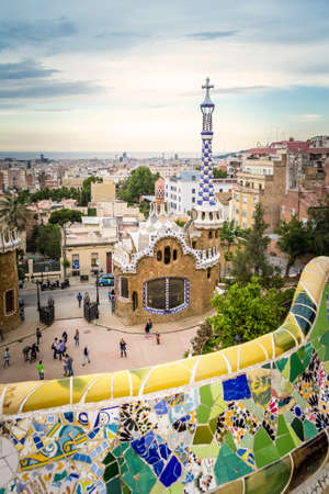 Famous colorful ceramic mosaic bench of park Guell, with entrance pavilion on the background  Designed by Antonio Gaudi and located in Barcelona, Spainのeditorial素材