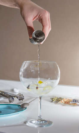 Closeup of barman hand pouring alcoholic drink with a jigger on glass to prepare gin tonic cocktail