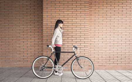 Beautiful young sportive woman posing with custom fixie bike over a orange brick wall on the...
