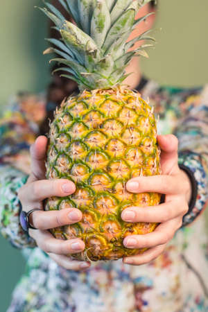 Colorful fashion girl portrait holding a pineapple between her hands over green backgroundの写真素材