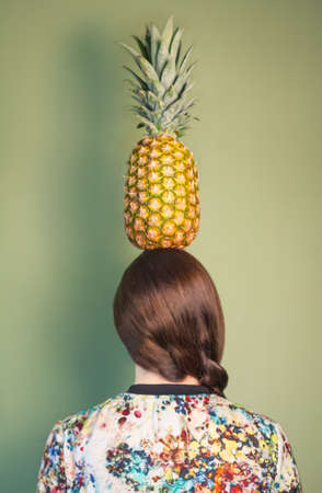 Back view of colorful fashion girl holding a pineapple over her head on green backgroundの写真素材
