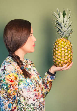 Colorful fashion girl portrait looking a pineapple in her hand over green backgroundの写真素材