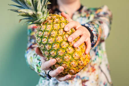 Colorful fashion girl portrait holding a pineapple between her hands over green backgroundの写真素材
