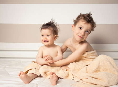 Portrait of sweet boy and little girl with wet hair under the towels playing over a bed after bathの写真素材